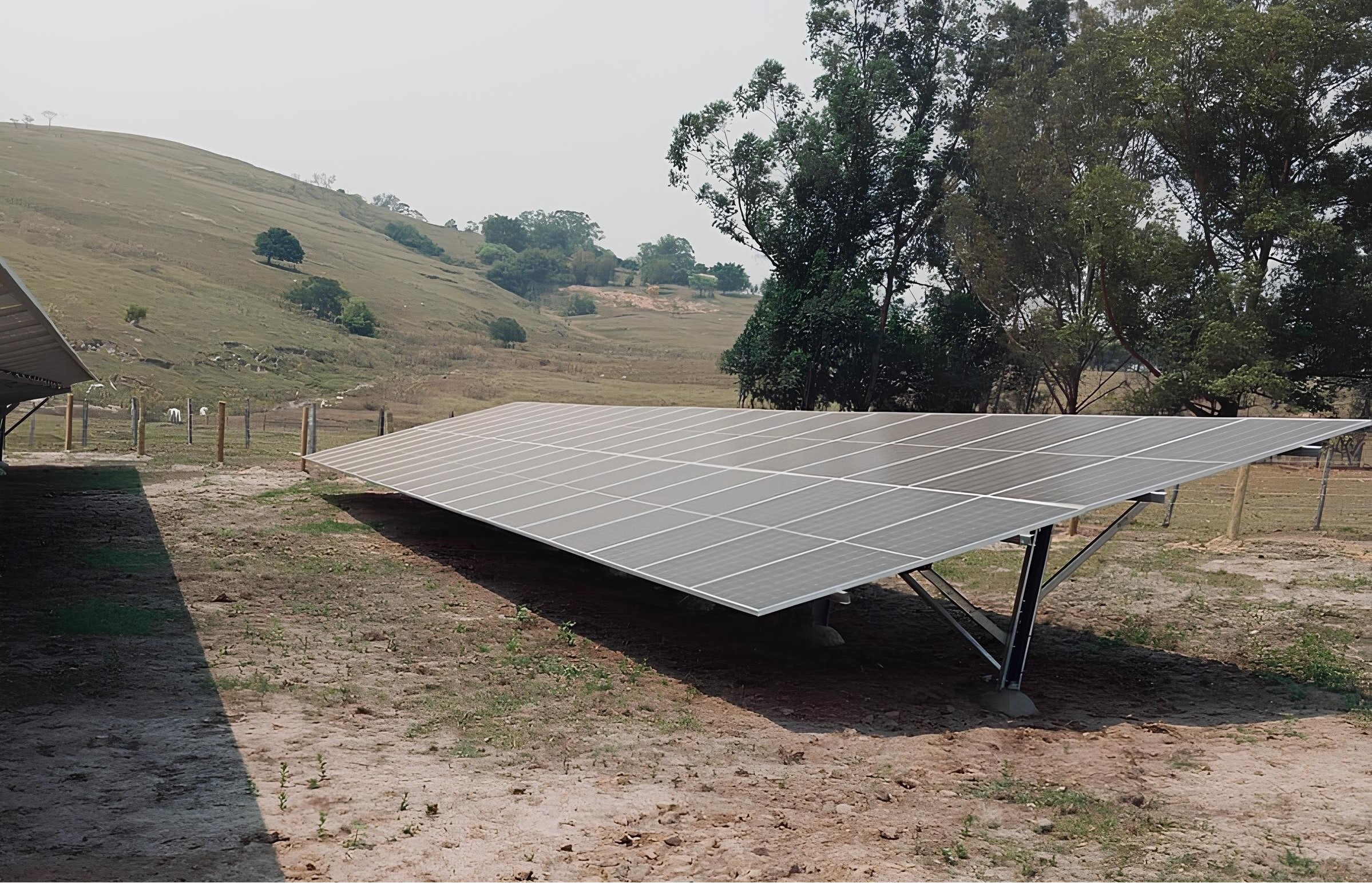 Painéis solares instalados em uma área rural com paisagem natural e árvores ao fundo.